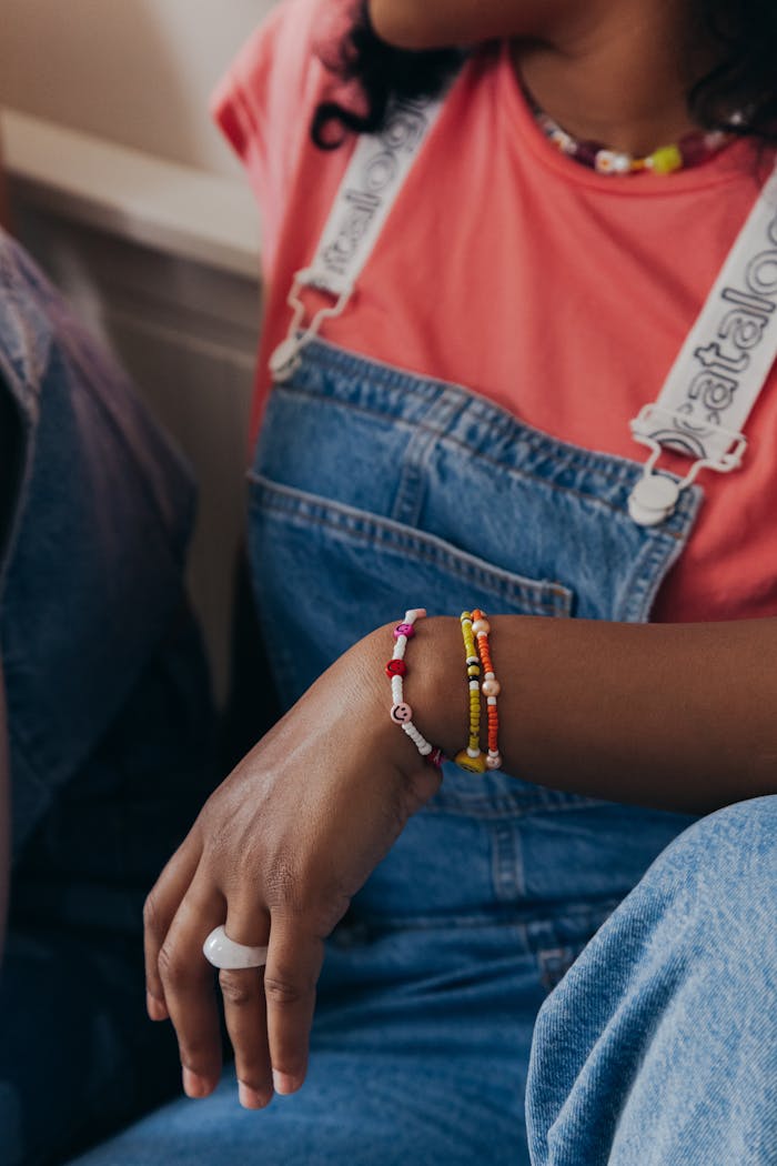 Close-up of a woman wearing beaded bracelets and denim overalls, showcasing casual fashion.