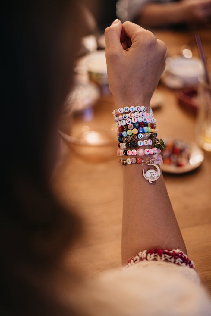 Vertical close-up shot of colorful handmade bracelets on a woman's arm with a blurred background.